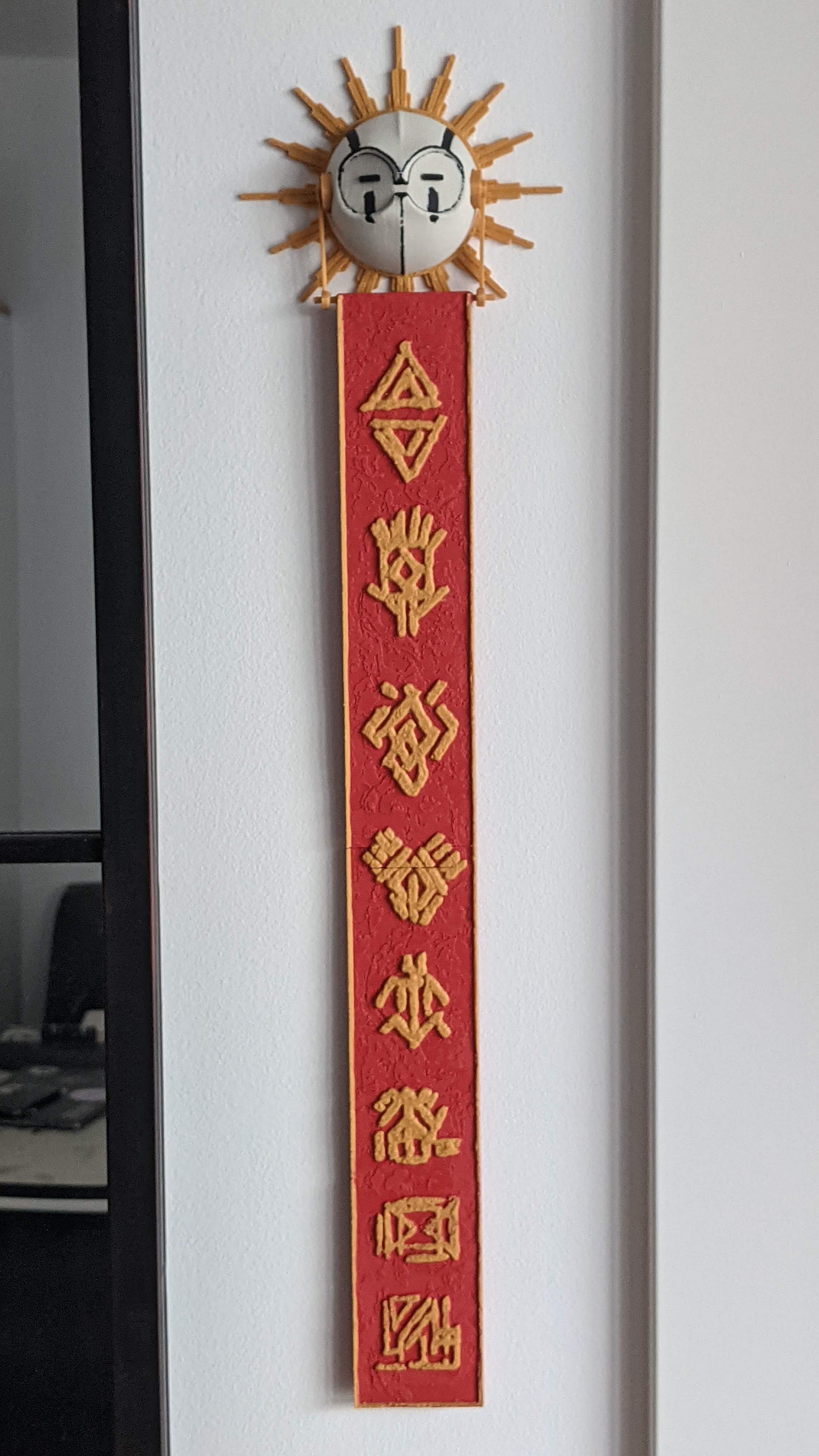 Decorative red banner with gold text and sun design on a white wall.