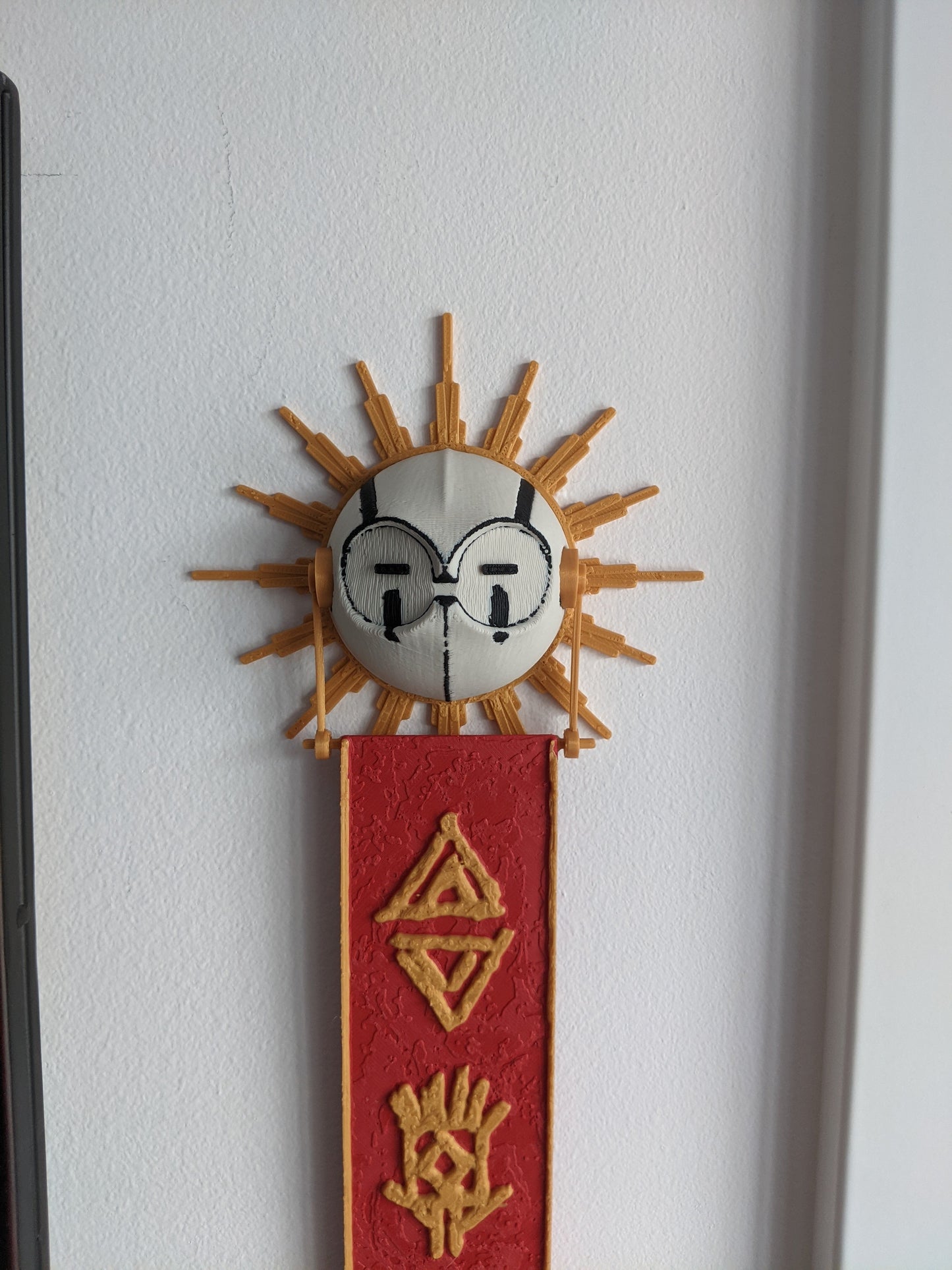 Decorative wall piece with sun design and red banner on a white wall