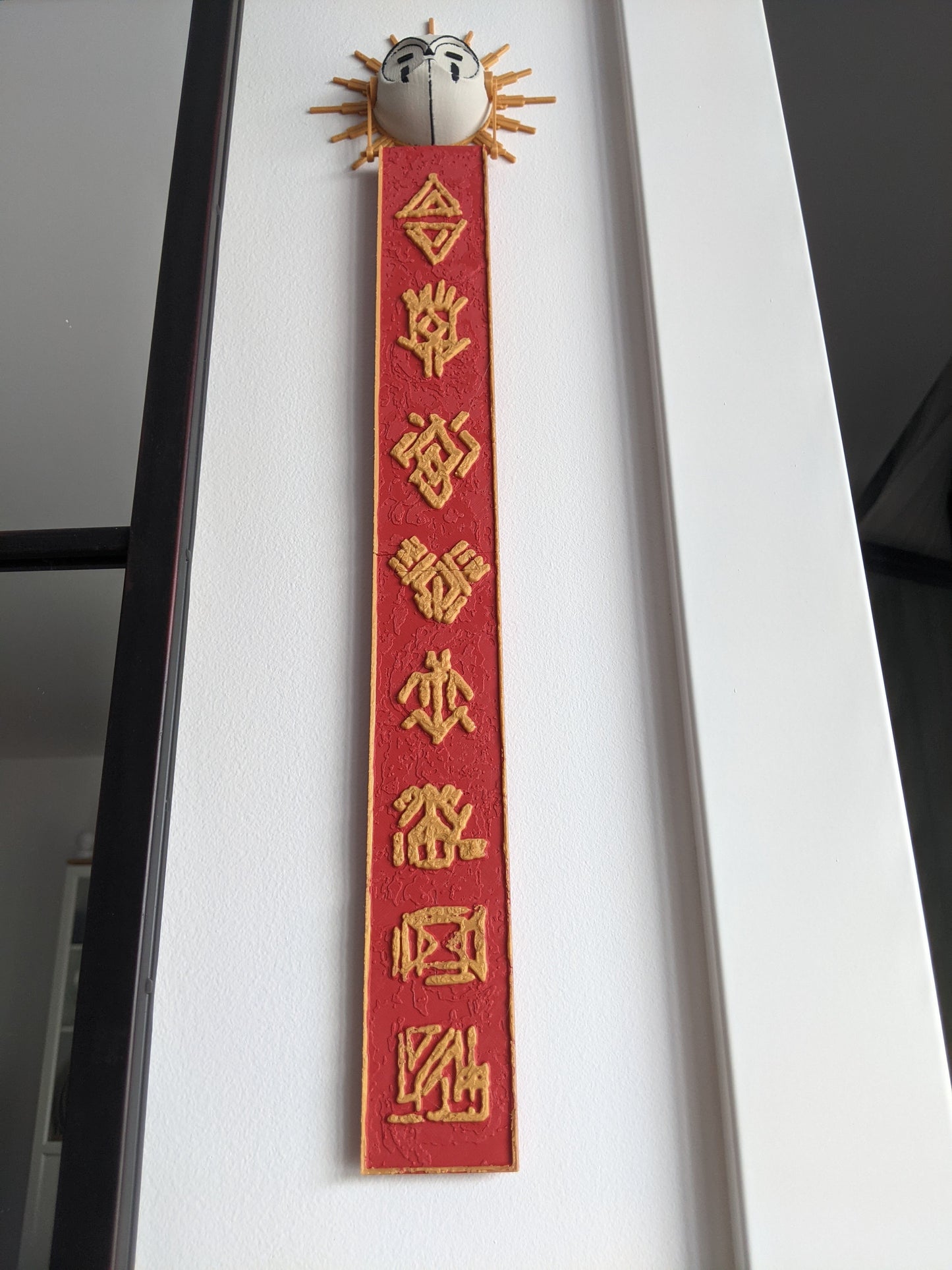 Decorative red ribbon with gold text and a small decorative object on top against a white background