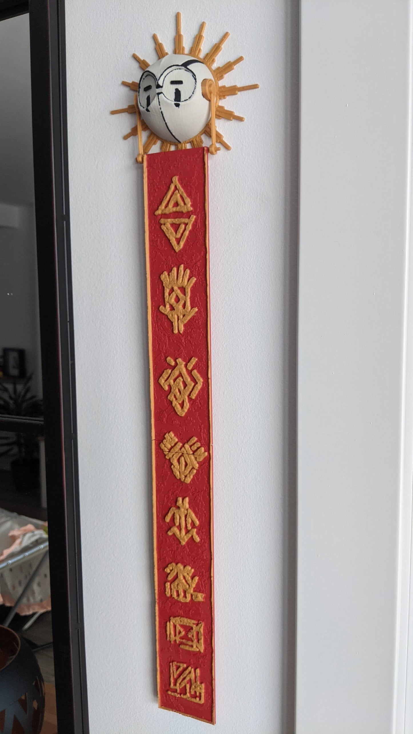 Decorative wall piece with a sun emblem and red banner on a white wall.