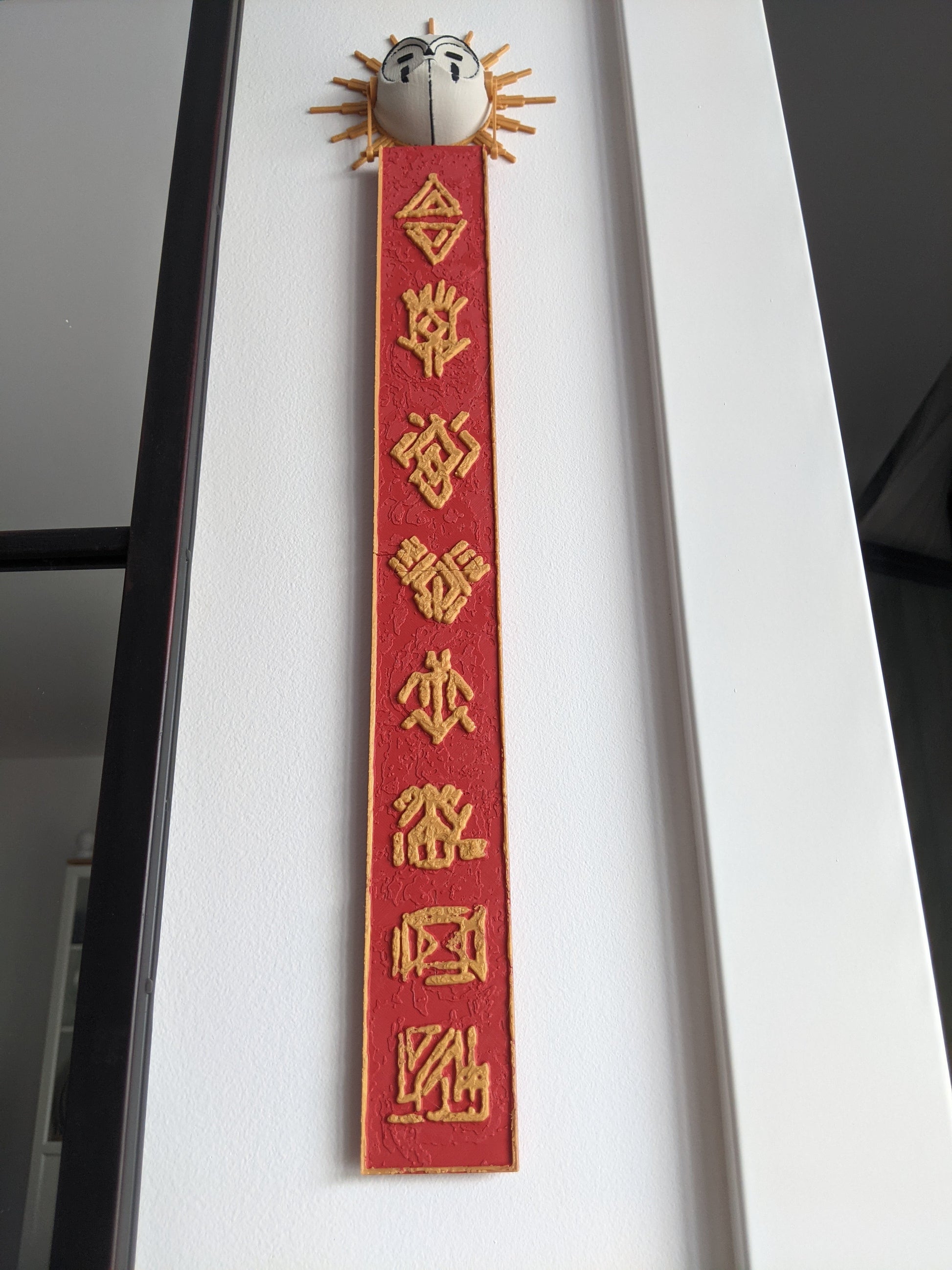 Decorative red ribbon with gold text and a small decorative object on top against a white background